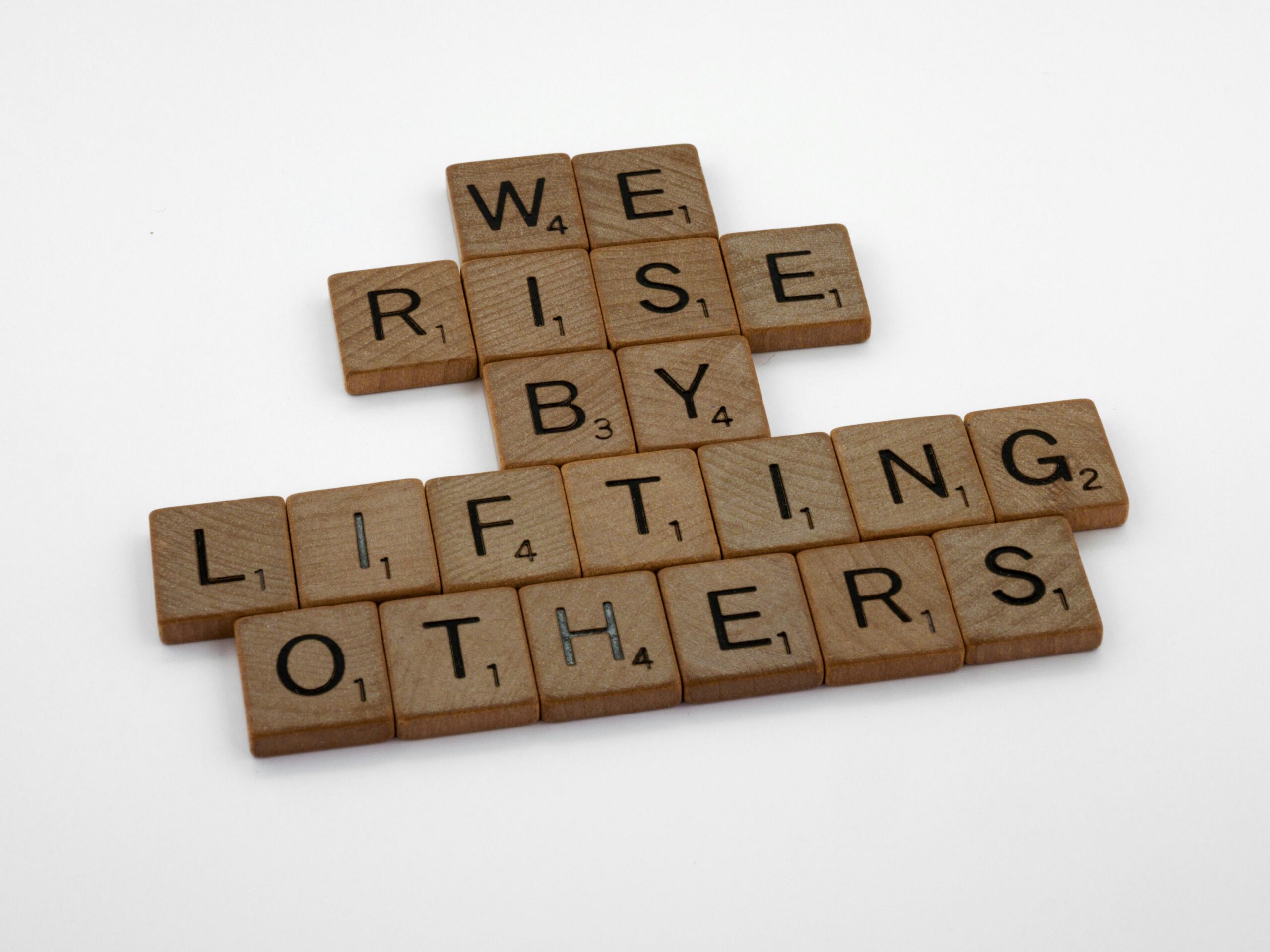 Scrabble tiles forming the quote &amp;amp;#039;We rise by lifting others&amp;amp;#039; on a white background.